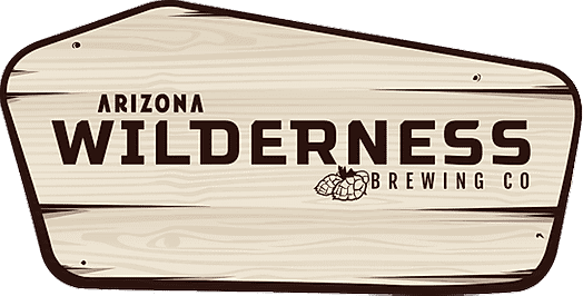 A wooden sign with the text Arizona Wilderness Brewing Co in dark letters and an illustration of hops beneath the word Wilderness.