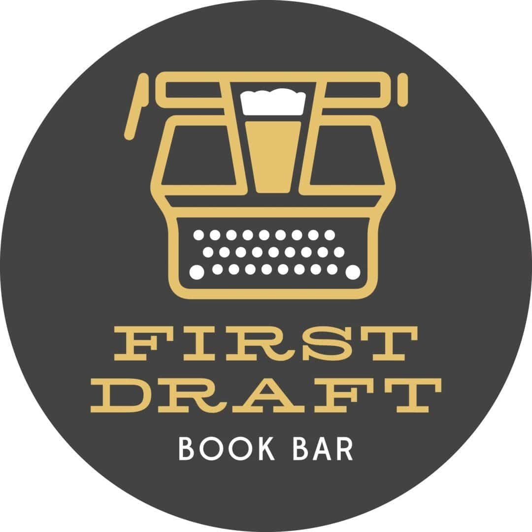 A circular logo with a gold typewriter design featuring a beer glass in the center, and the words FIRST DRAFT BOOK BAR below on a dark background.