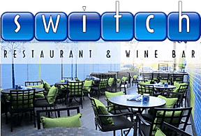 Outdoor patio seating at Switch Restaurant & Wine Bar, featuring round tables with black chairs and green cushions, with the restaurants blue and white logo above the scene.